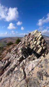 A man in a hat is walking across a rocky ridge